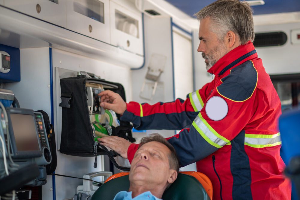 medical repatriation Service being provided by a Focused paramedic standing behind an unconscious man and turning the knob on the breathing apparatus