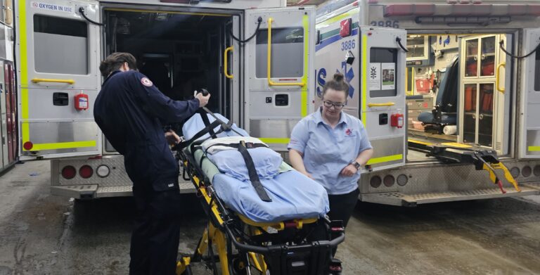 Two paramedics preparing a stretcher in the hallway of an emergency room in Alberta